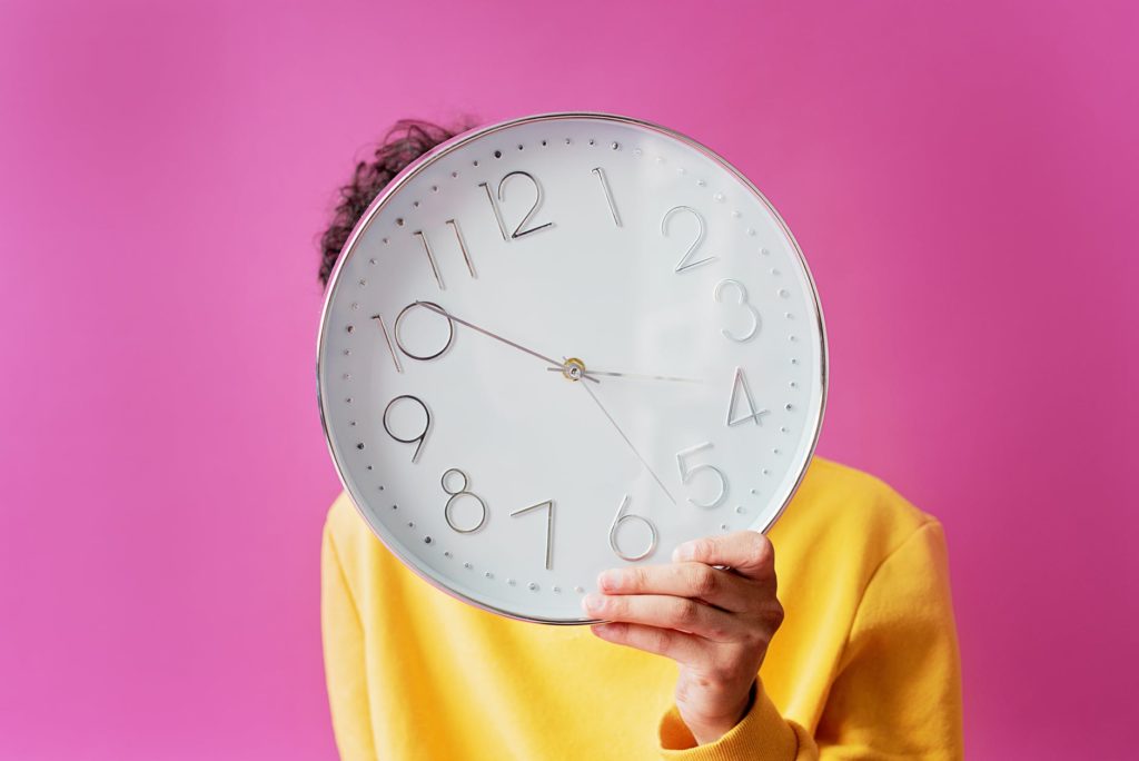 person holding wall clock in front of face
